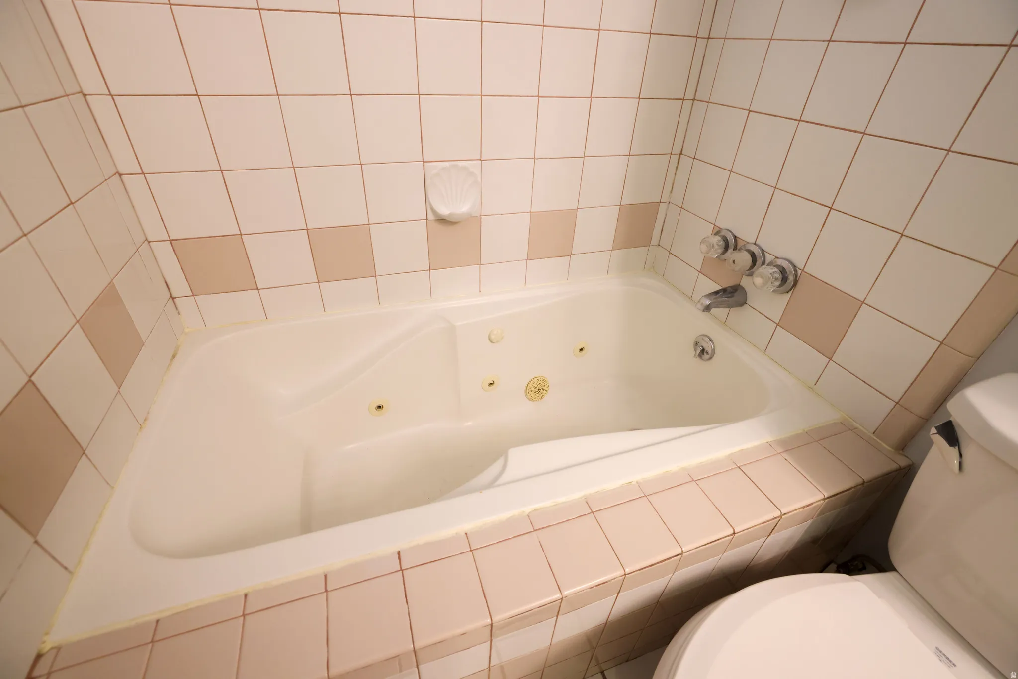 Jetted bathtub with white ceramic tile surround and wall-mounted chrome fixtures
