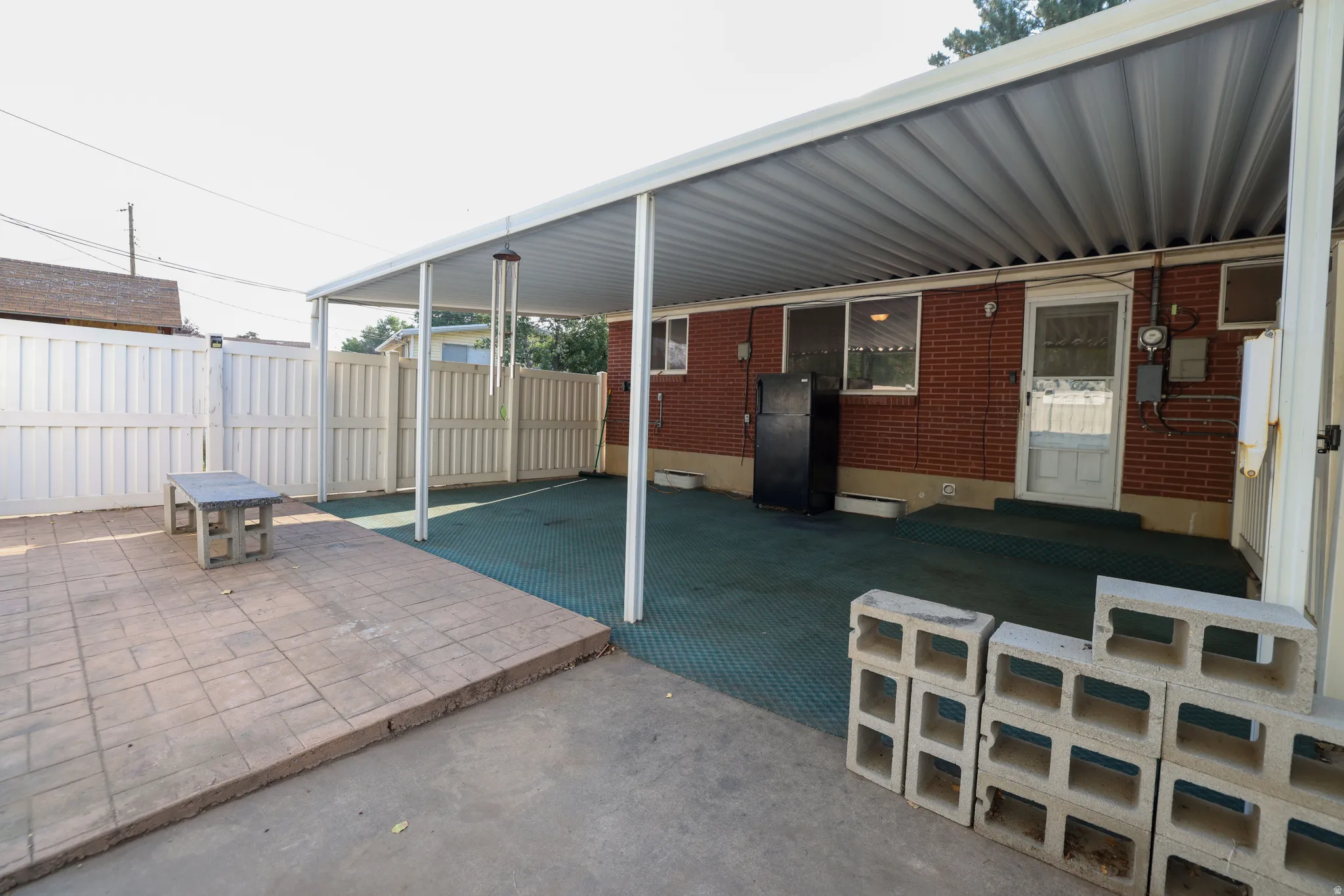 Covered patio with a corrugated metal roof, brick exterior, and a privacy fence