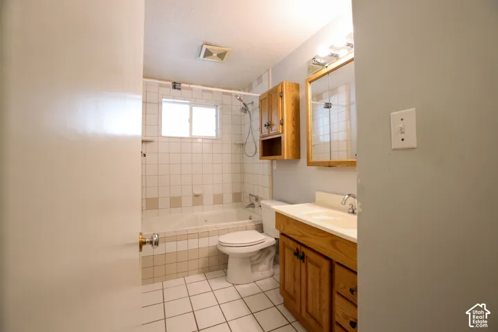 Bathroom featuring a built-in tub with tile surround, a single window, and a wood-finish vanity with an integrated sink
