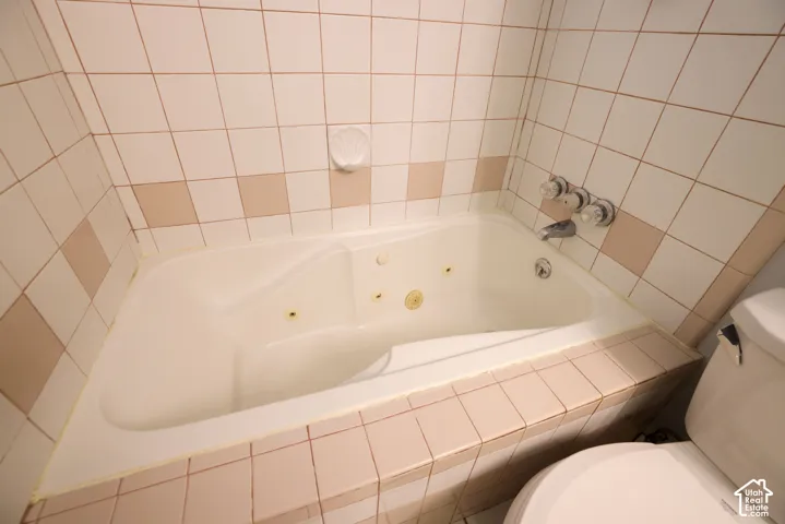 Jetted bathtub with white ceramic tile surround and wall-mounted chrome fixtures