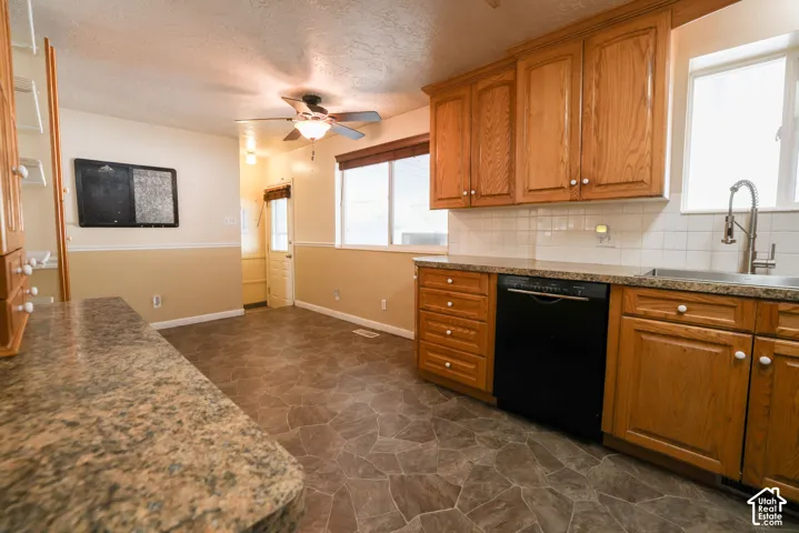 Spacious kitchen featuring wood cabinetry, stainless steel appliances including a black dishwasher, dual sink with chrome faucet, subway tile backsplash, and stone-finish flooring throughout