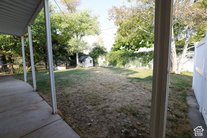 Covered patio with concrete flooring, fenced yard, mature trees, and a storage shed