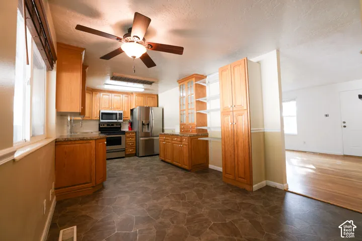 Kitchen featuring wood-finish cabinetry, stainless steel appliances, a ceiling fan, and stone-look flooring