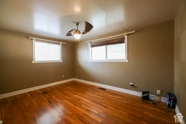 Hardwood flooring, two windows with blinds, ceiling fan with integrated lighting, and neutral wall paint