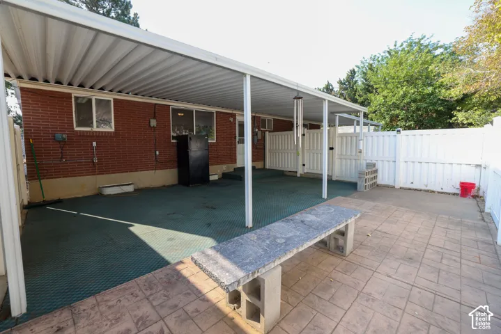 Covered patio area with a brick exterior, concrete pavers, and white privacy fencing