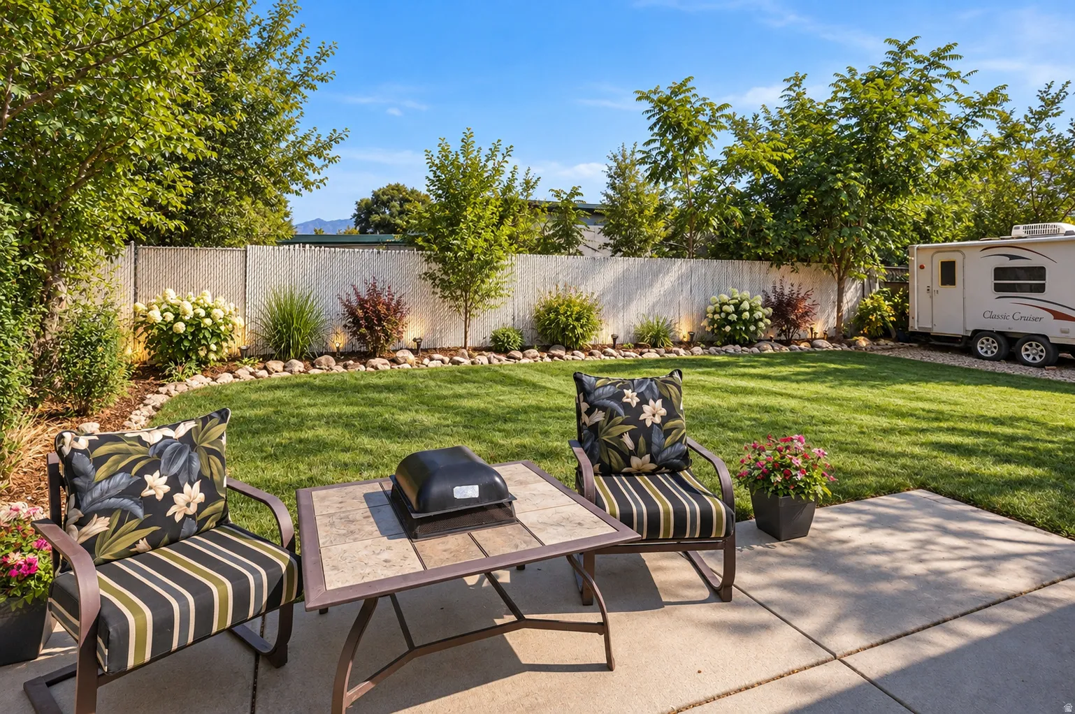 Private backyard featuring a concrete patio, manicured lawn, and perimeter landscaping with decorative rock borders