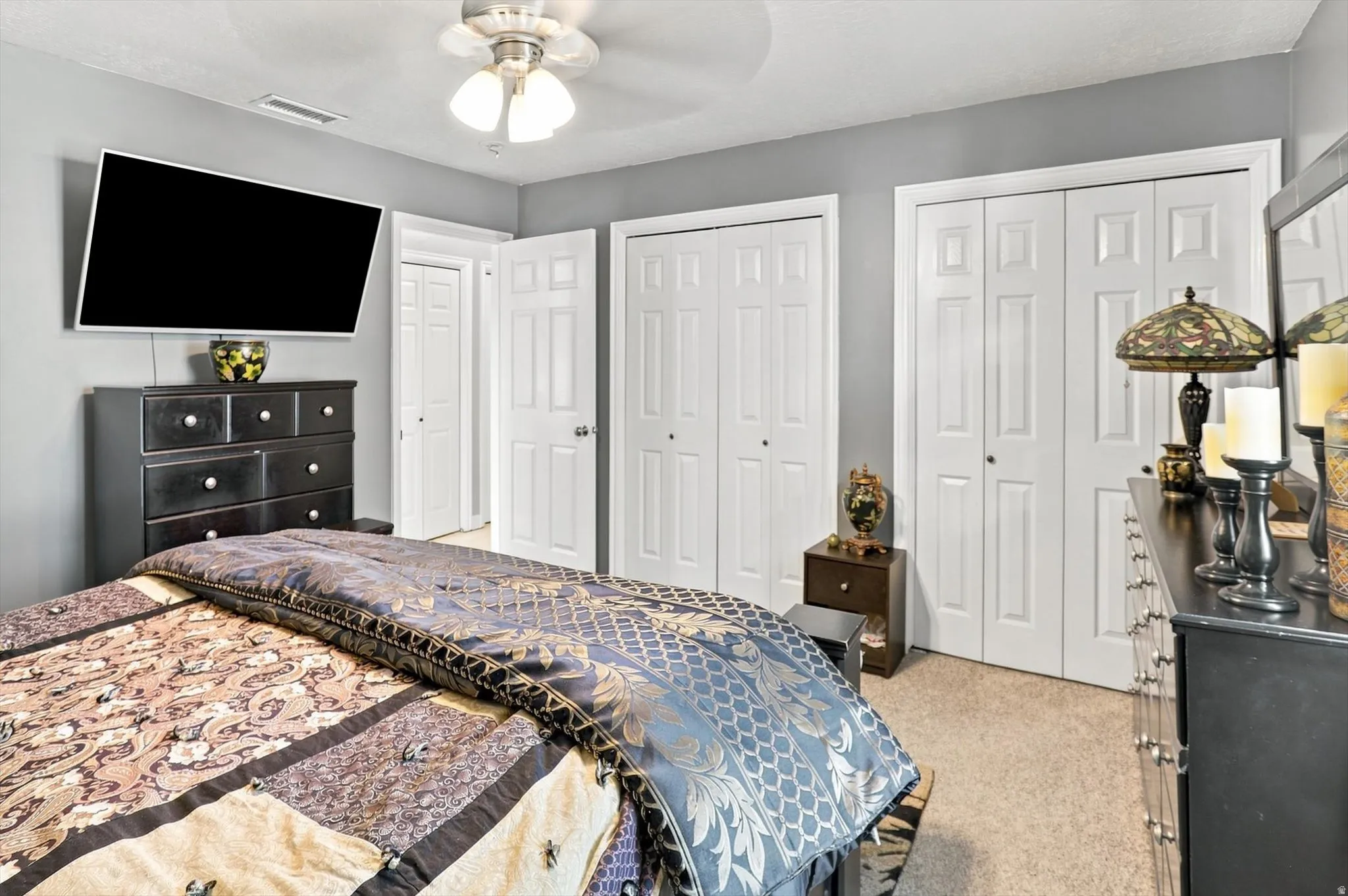 Neutral wall color, ceiling fan with integrated lighting, multiple paneled closet doors, carpeted flooring