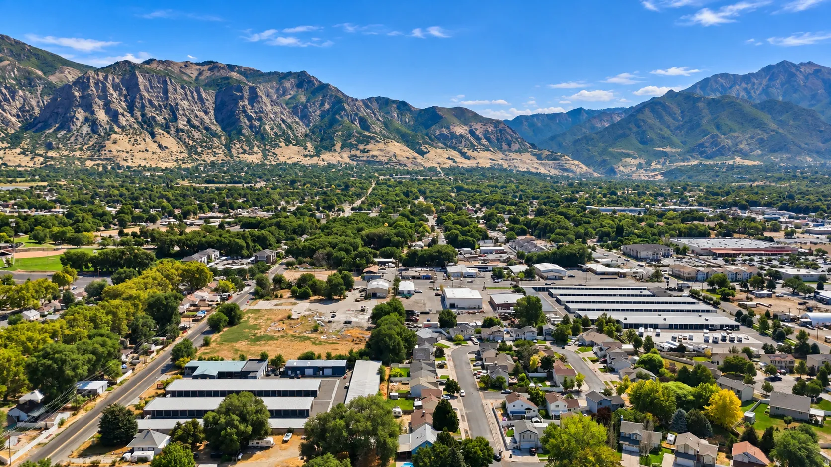 Expansive mountain backdrop with a wide urban area featuring numerous residential properties, commercial structures, and mature trees