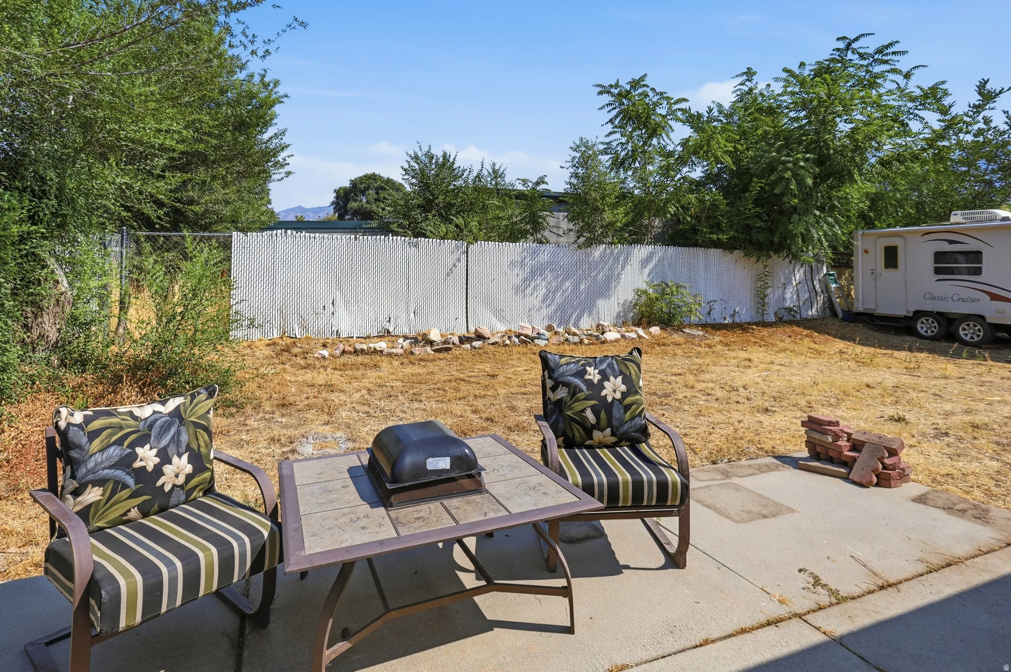 Patio area with concrete pavers, perimeter fencing, and mature trees