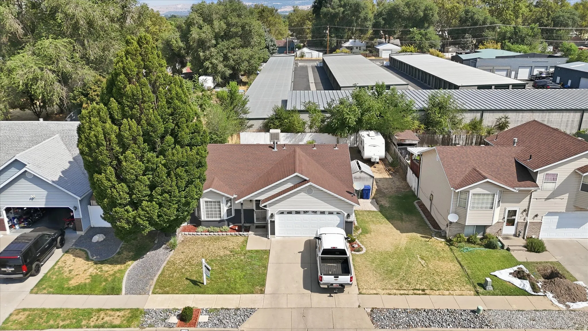 Single-story residence featuring a two-car garage, front yard landscaping with a gravel path, and mature trees