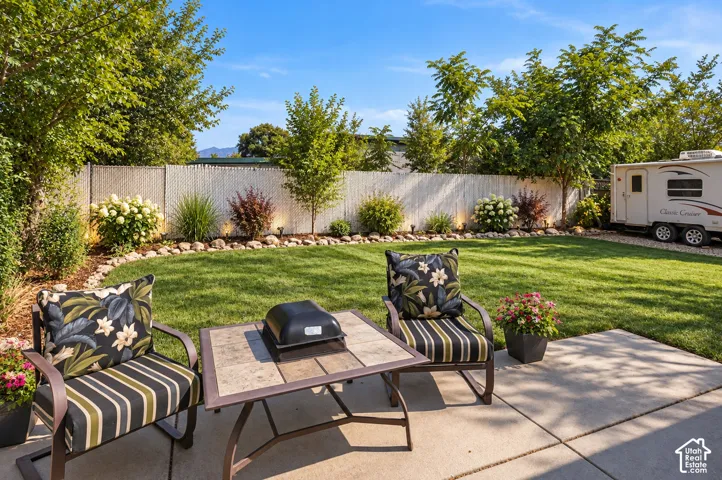 Private backyard featuring a concrete patio, manicured lawn, and perimeter landscaping with decorative rock borders