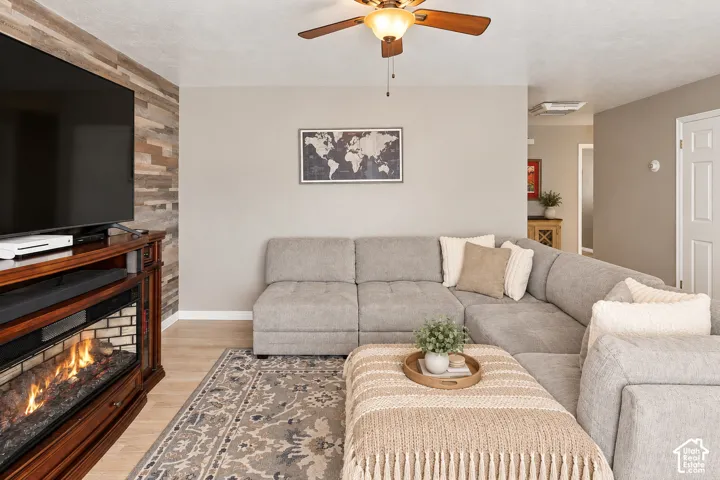 Accent wall featuring wood paneling, wood-finish flooring, ceiling fan, and an electric fireplace with a wood mantel