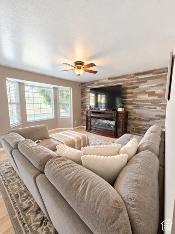 Bay window with blinds, wood-finish flooring, accent wall with horizontal wood paneling, and a ceiling fan with integrated lighting