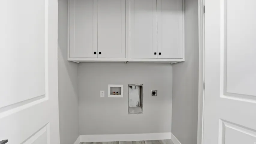 Dedicated laundry area featuring white shaker-style cabinetry with matte black hardware, light gray walls, and wood-finish flooring