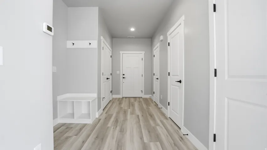 Inviting hallway with light wood-finish flooring, recessed lighting, and crisp white trim