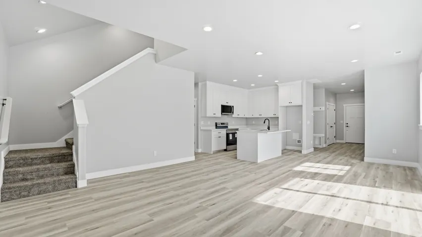 Open-concept living space featuring wood-finish flooring, recessed lighting, a kitchen island with seating, white shaker cabinetry, and stainless steel appliances