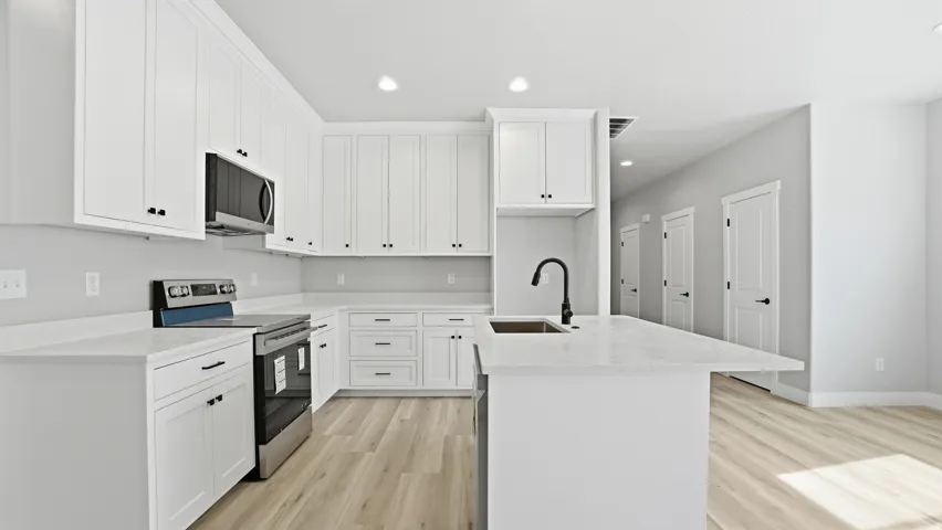 Modern kitchen featuring white shaker cabinetry, light countertops, stainless steel appliances, and wood-finish flooring