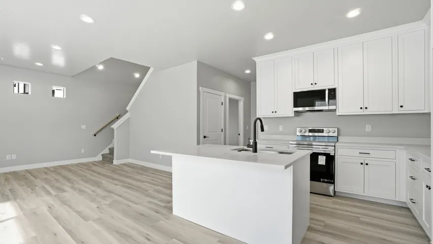 Open-concept living space featuring a kitchen island with sink, white shaker cabinetry, stainless steel appliances, and light wood-finish flooring