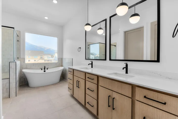 Freestanding soaking tub with a large picture window, dual vanity with wood-finish cabinetry, white countertops, and matte black fixtures, and a walk-in shower with a glass enclosure