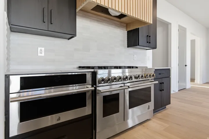 Stainless steel range with multiple burners, double ovens, built-in microwave, dark wood-finish cabinetry, and a textured tile backsplash