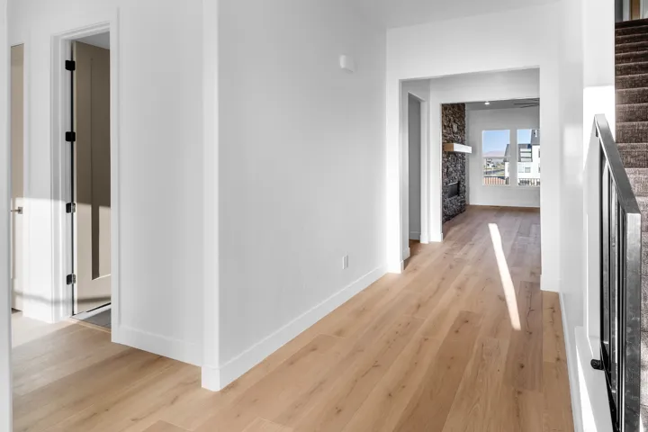 Wide plank wood-finish flooring throughout, leading to an open living area featuring a stone-clad fireplace with a natural wood mantel