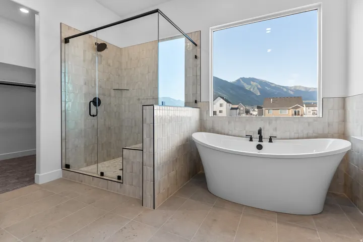 Freestanding soaking tub with a large window, glass-enclosed shower with a built-in bench, and floor-to-ceiling tile