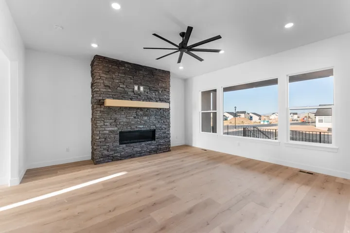 Wood-finish flooring, recessed lighting, and a stone-clad fireplace with a natural wood mantel