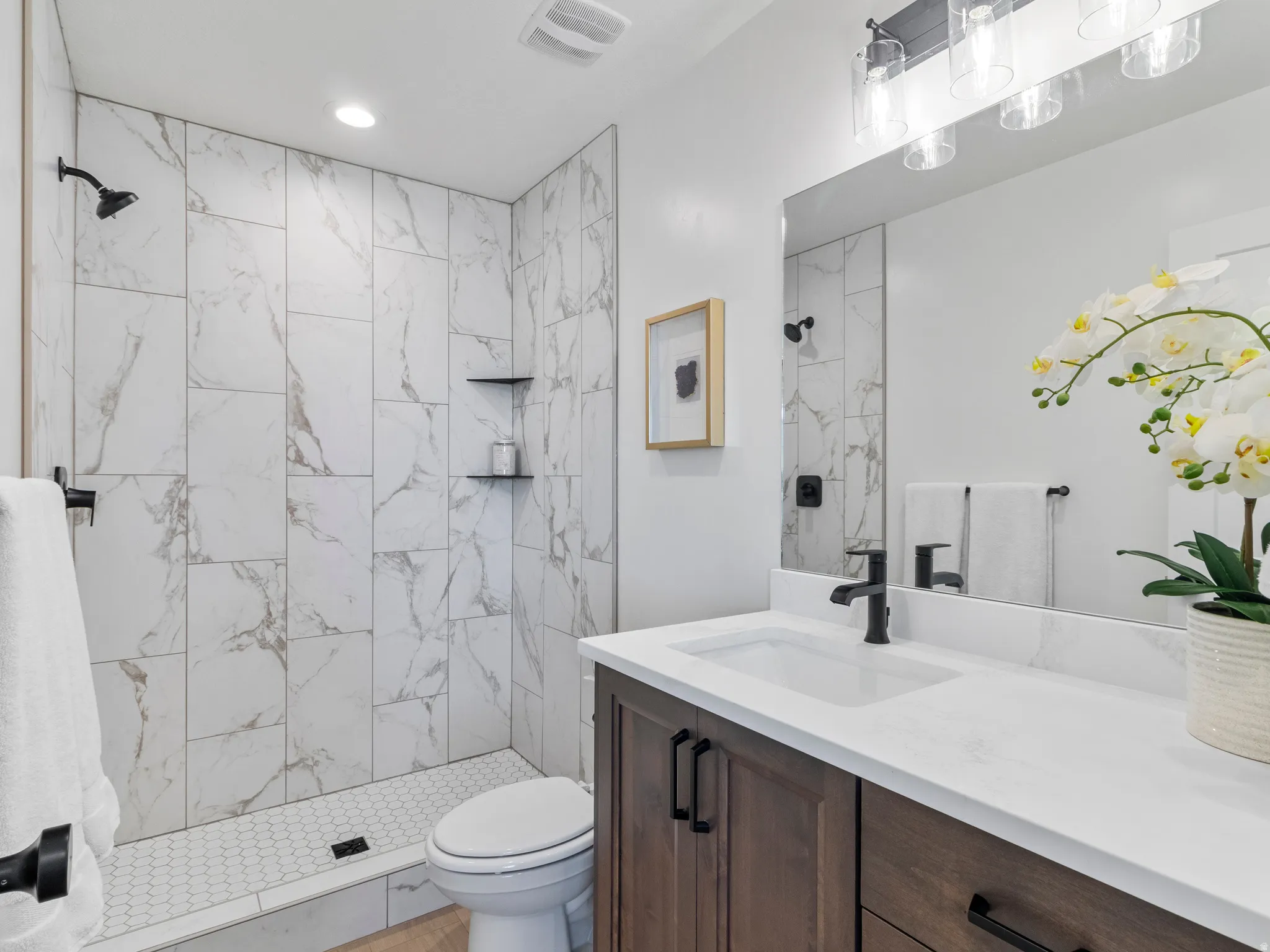 Walk-in shower with full-height marble-look tile surround and hex tile floor