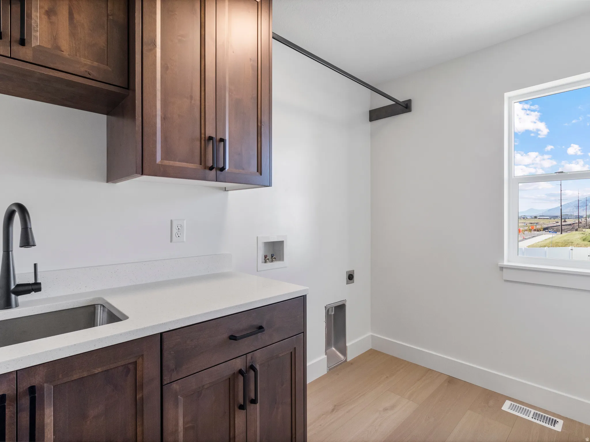 Built-in wood cabinetry, integrated stainless steel sink with matte black faucet, light-toned wood-finish flooring, and white countertops