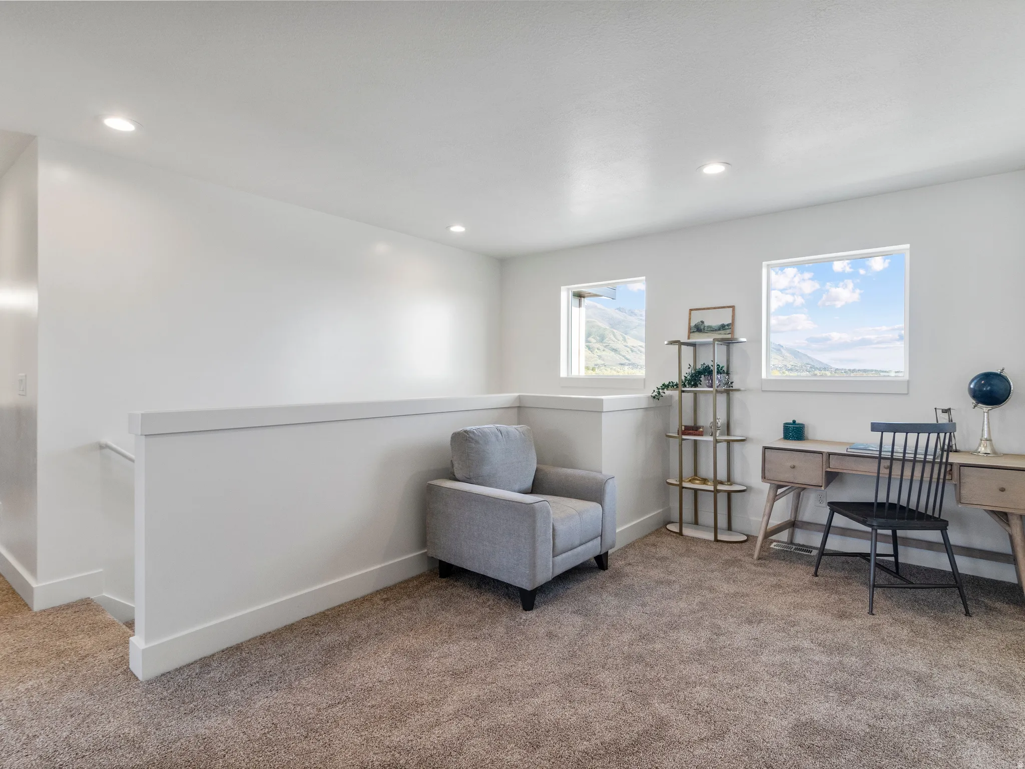 Recessed ceiling lighting, white walls, two windows, carpeted flooring, and a white half-wall railing