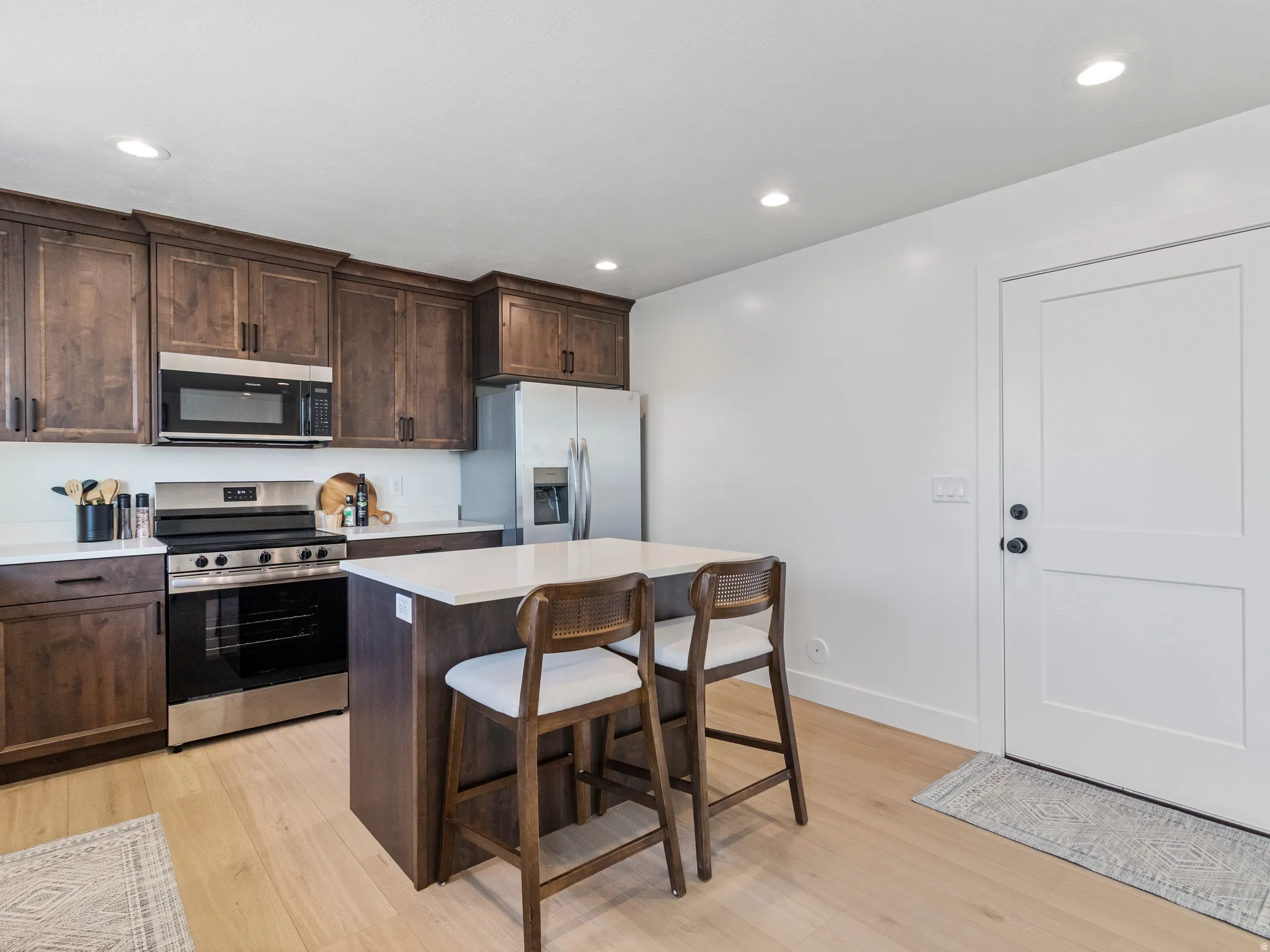 Kitchen featuring wood-finish cabinetry, stainless steel appliances, a center island with countertop seating, and light wood-finish flooring