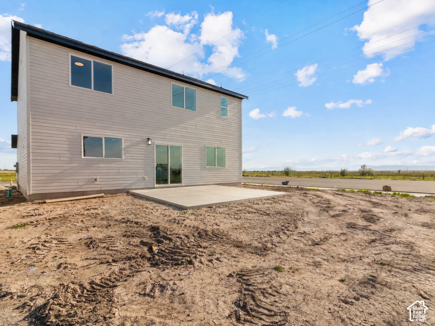 Light-colored horizontal siding, dark-colored roofline, multiple windows, and a concrete patio. AI was used to update the photo with the completed concrete.