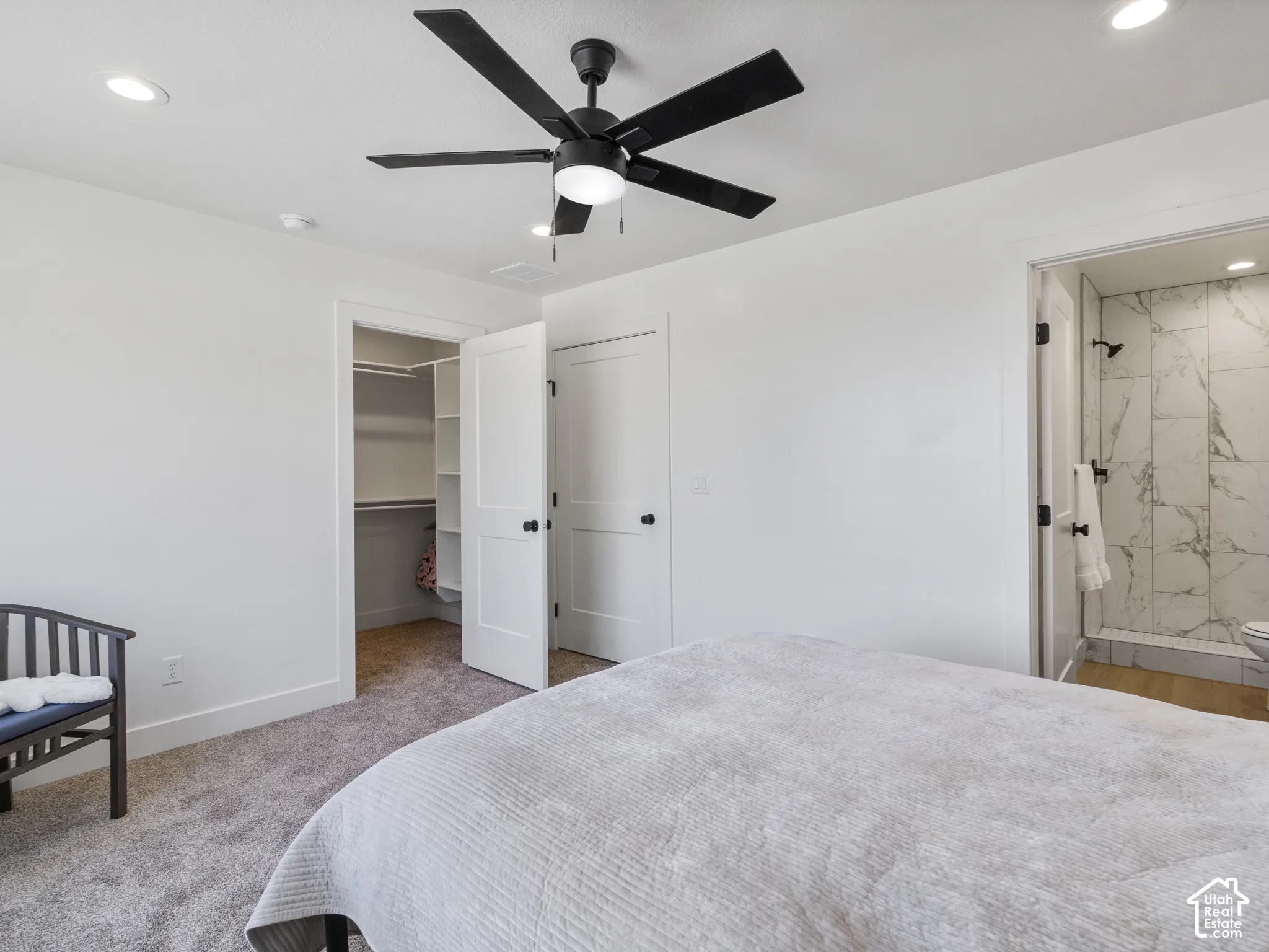 Recessed lighting, ceiling fan with integrated light, carpeted flooring, walk-in closet with shelving, and an en-suite bathroom featuring a tiled shower with matte black fixtures