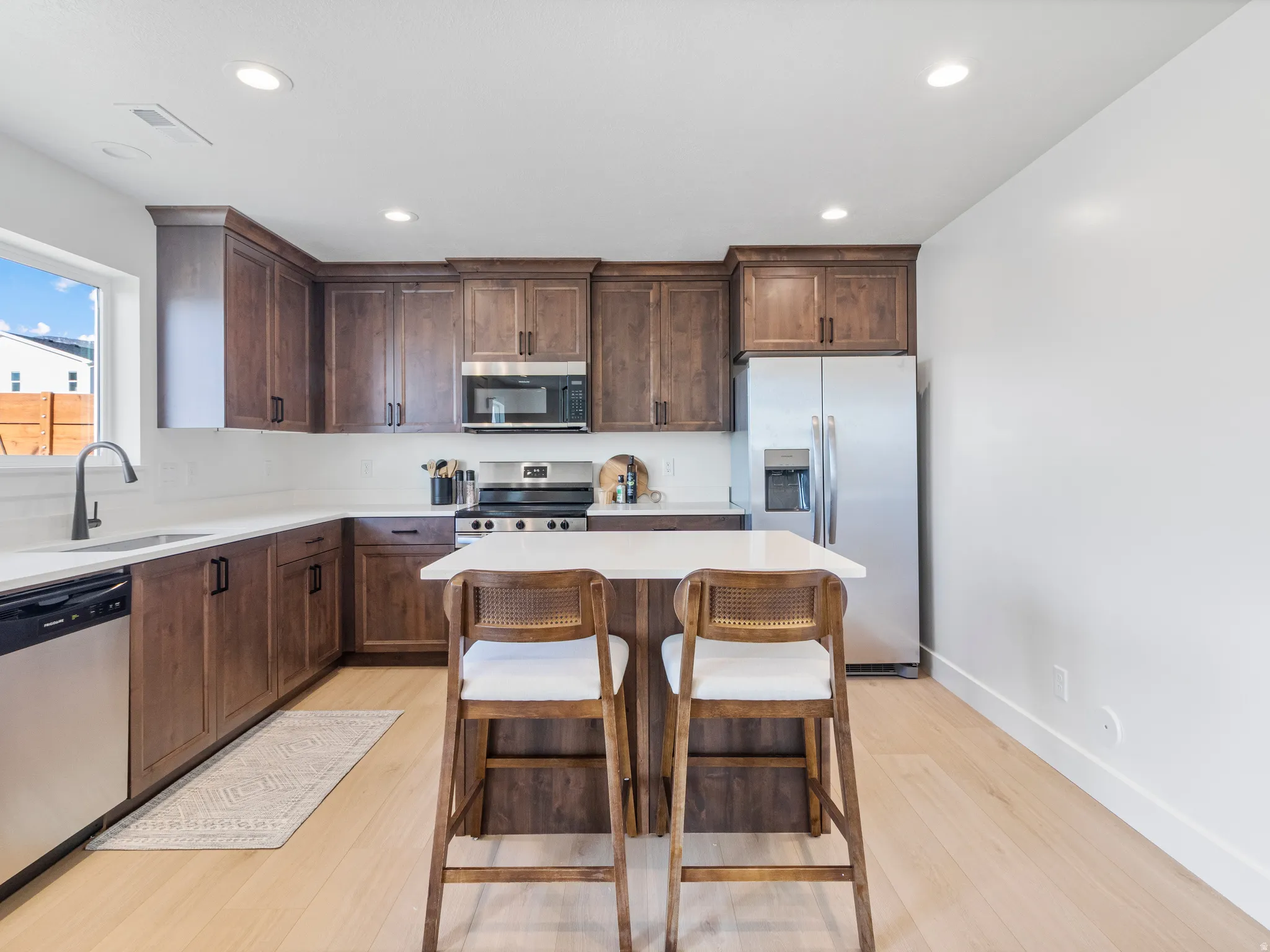 Kitchen featuring rich wood cabinetry, stainless steel appliances, light-toned wood-finish flooring, white countertops, and a central island with seating