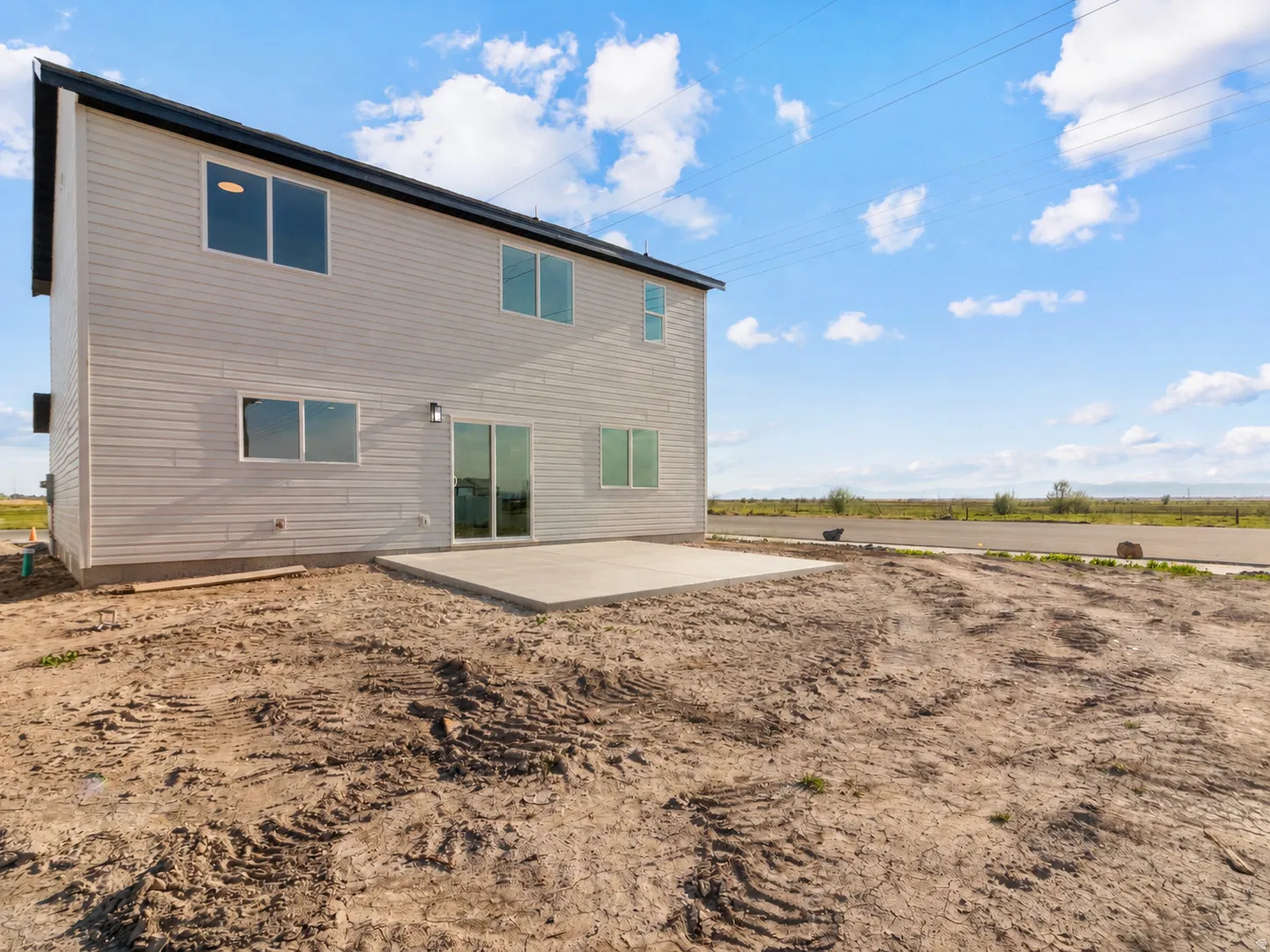 Light-colored horizontal siding, dark-colored roofline, multiple windows, and a concrete patio. AI was used to update the photo with the completed concrete.