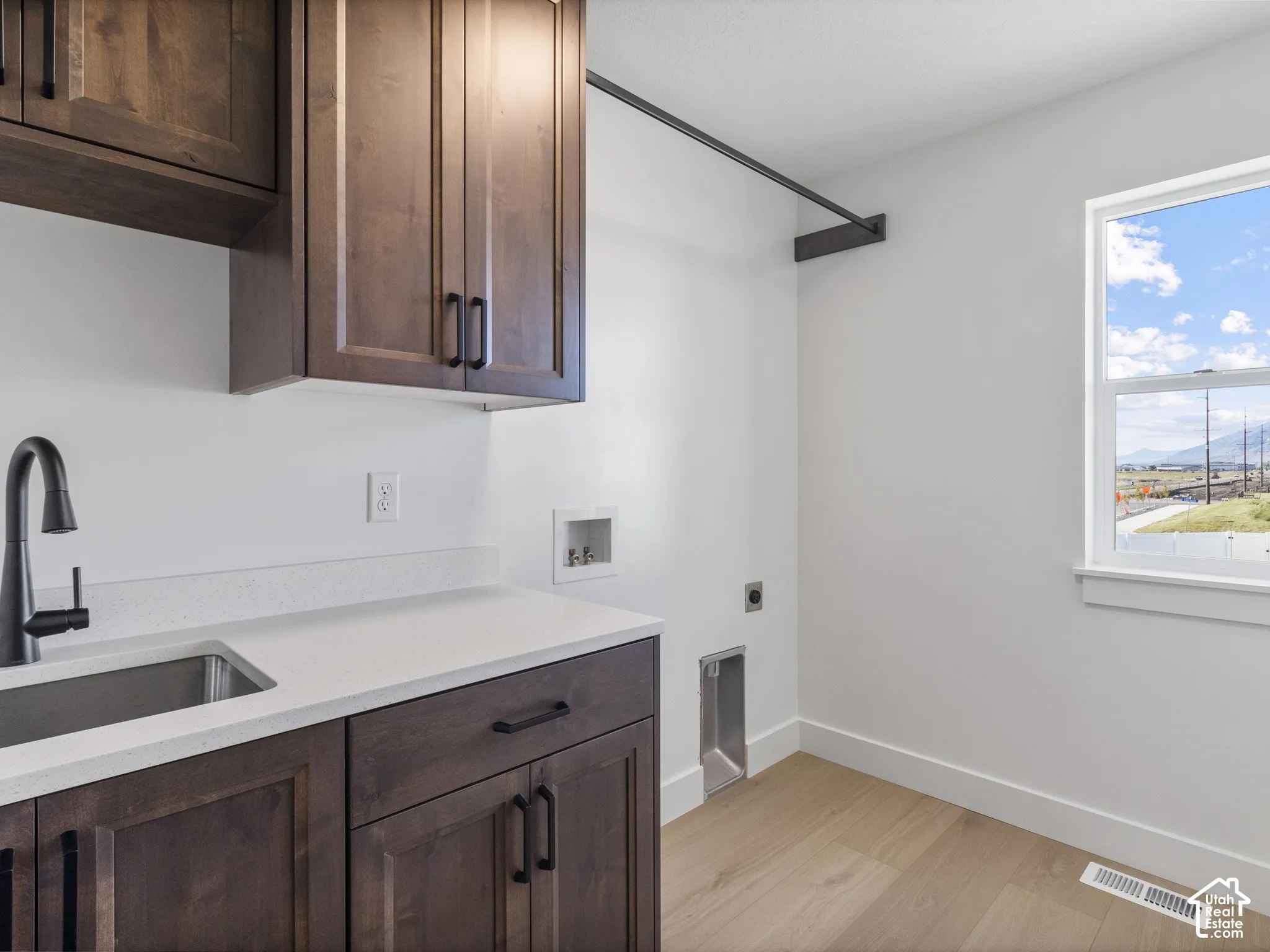 Built-in wood cabinetry, integrated stainless steel sink with matte black faucet, light-toned wood-finish flooring, and white countertops