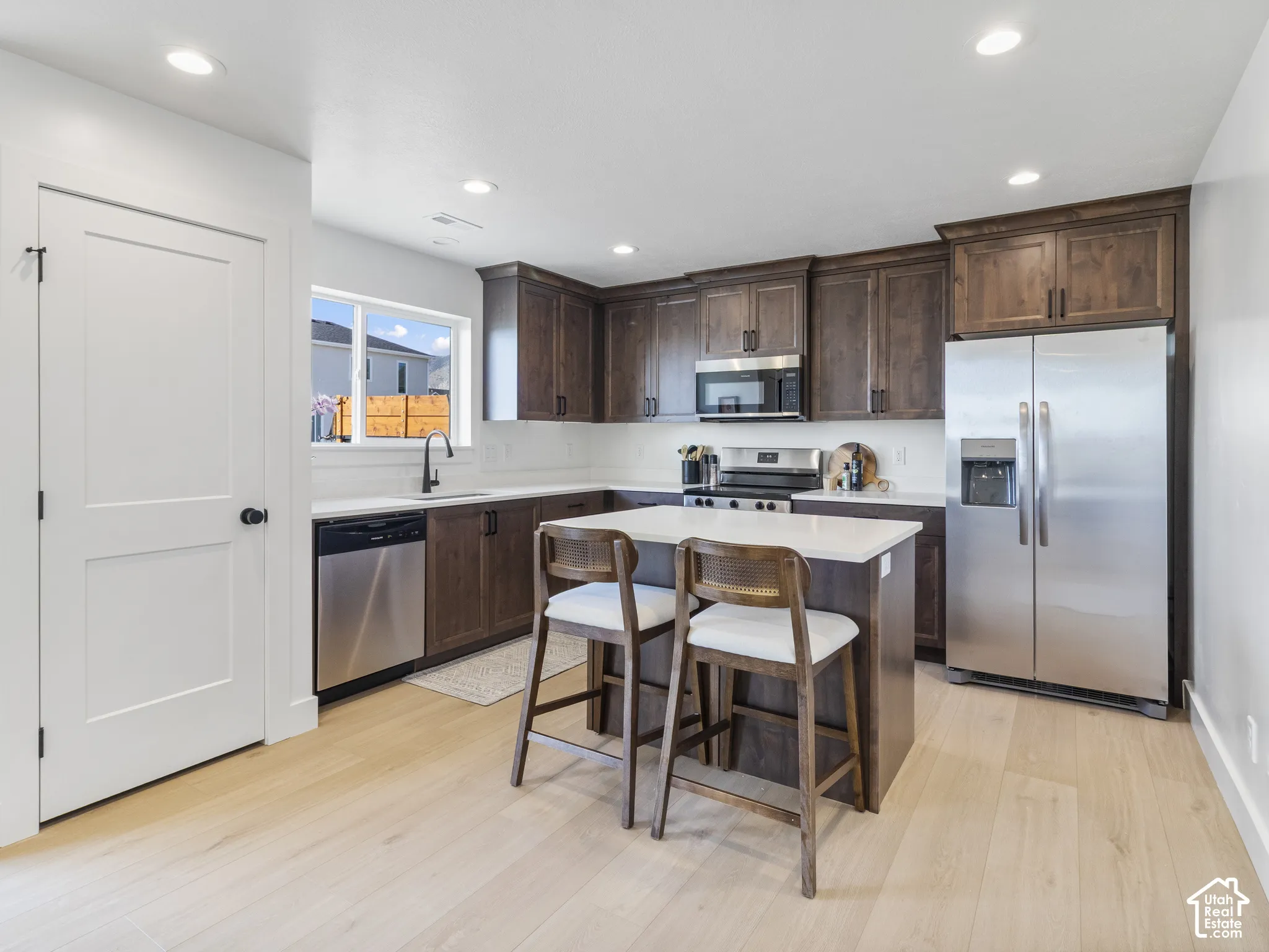 Kitchen featuring wood-finish flooring, recessed lighting, dark wood cabinetry, stainless steel appliances, and a central island with a light-toned countertop