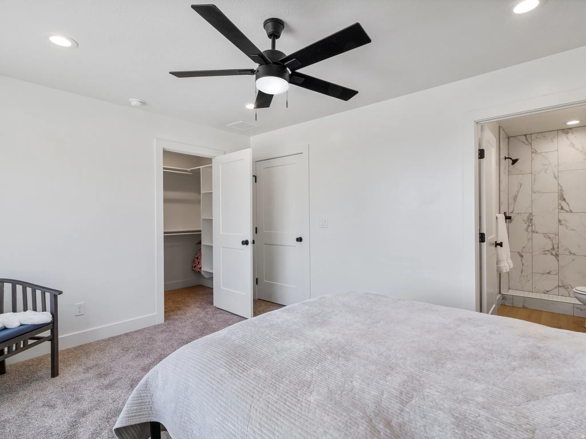 Recessed lighting, ceiling fan with integrated light, carpeted flooring, walk-in closet with shelving, and an en-suite bathroom featuring a tiled shower with matte black fixtures