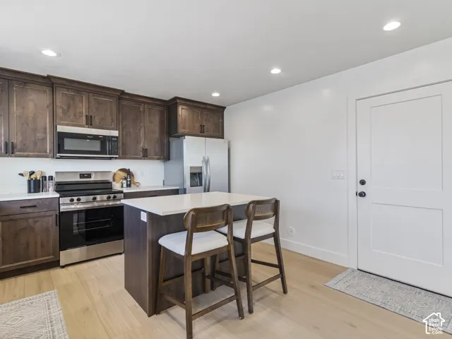 Kitchen featuring wood-finish cabinetry, stainless steel appliances, a center island with countertop seating, and light wood-finish flooring