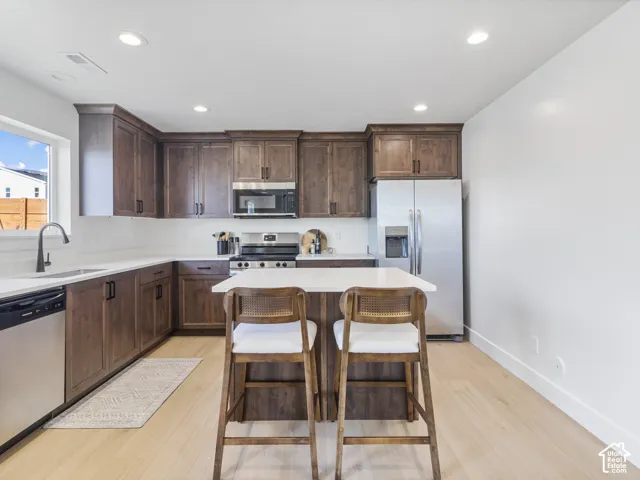 Kitchen featuring rich wood cabinetry, stainless steel appliances, light-toned wood-finish flooring, white countertops, and a central island with seating
