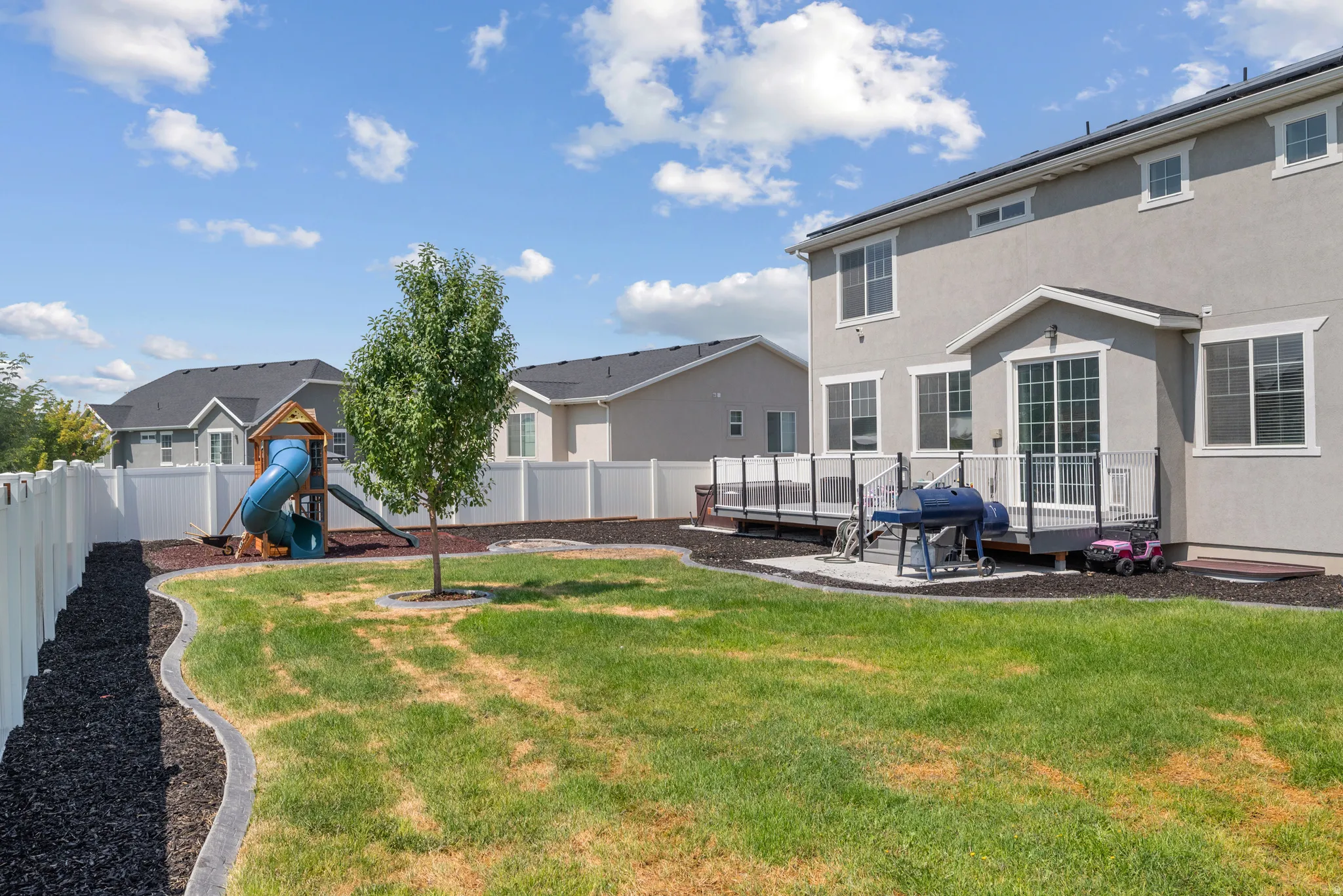 Spacious backyard featuring a built-in multi-level deck with a glass railing system, a white privacy fence, and a mature tree