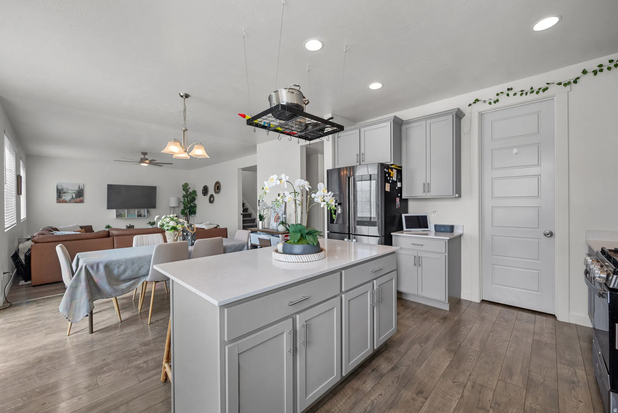 Kitchen island with a light-toned countertop, gray cabinetry, wood-finish flooring, recessed lighting, and a pot rack