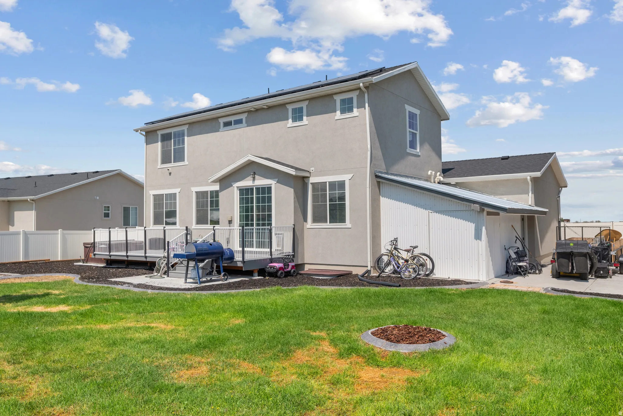Expansive green lawn, multi-level deck with dark railing, white vinyl privacy fencing, stucco exterior, and a detached shed with a metal roof