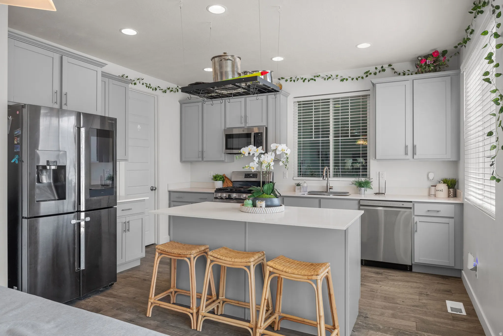 Kitchen featuring wood-finish flooring, recessed lighting, light gray cabinetry, stainless steel appliances, and a central island with a white countertop