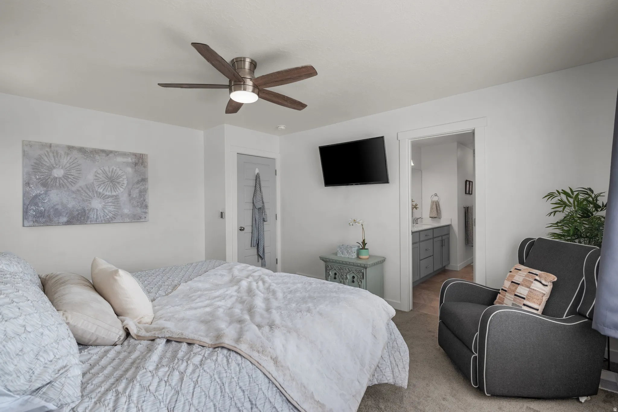 Bedroom with a ceiling fan, wall-mounted television, and an open doorway leading to a bathroom featuring a vanity with a sink