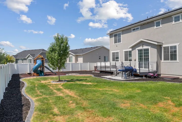 Spacious backyard featuring a built-in multi-level deck with a glass railing system, a white privacy fence, and a mature tree