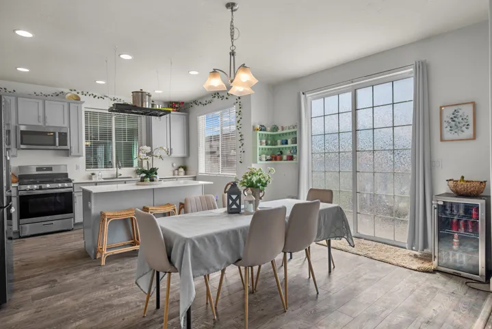Contemporary kitchen and dining area featuring wood-finish flooring, a kitchen island with seating, light gray cabinetry, stainless steel appliances, and a sliding glass door