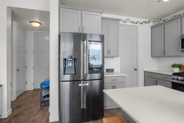Stainless steel French door refrigerator, light gray shaker-style cabinetry, light-toned countertops, and wood-finish flooring