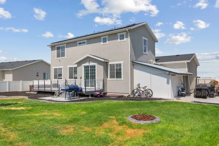 Expansive green lawn, multi-level deck with dark railing, white vinyl privacy fencing, stucco exterior, and a detached shed with a metal roof