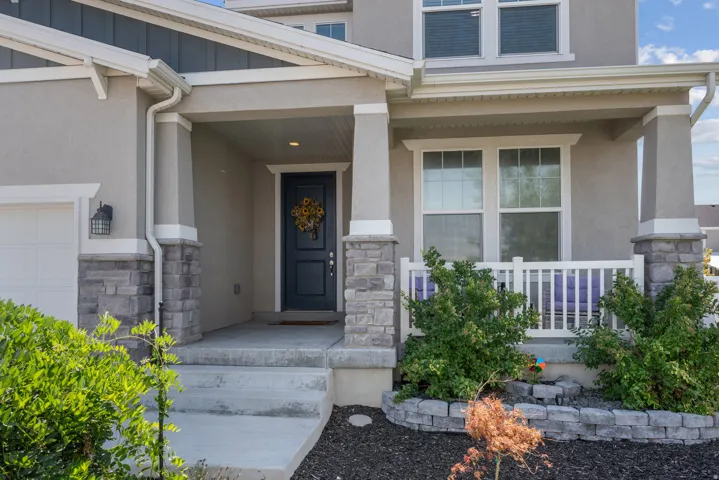 Front porch with white railing, stone column bases, and a dark paneled entry door